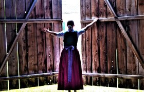 A woman in traditional dress opens large wooden doors to the outside.