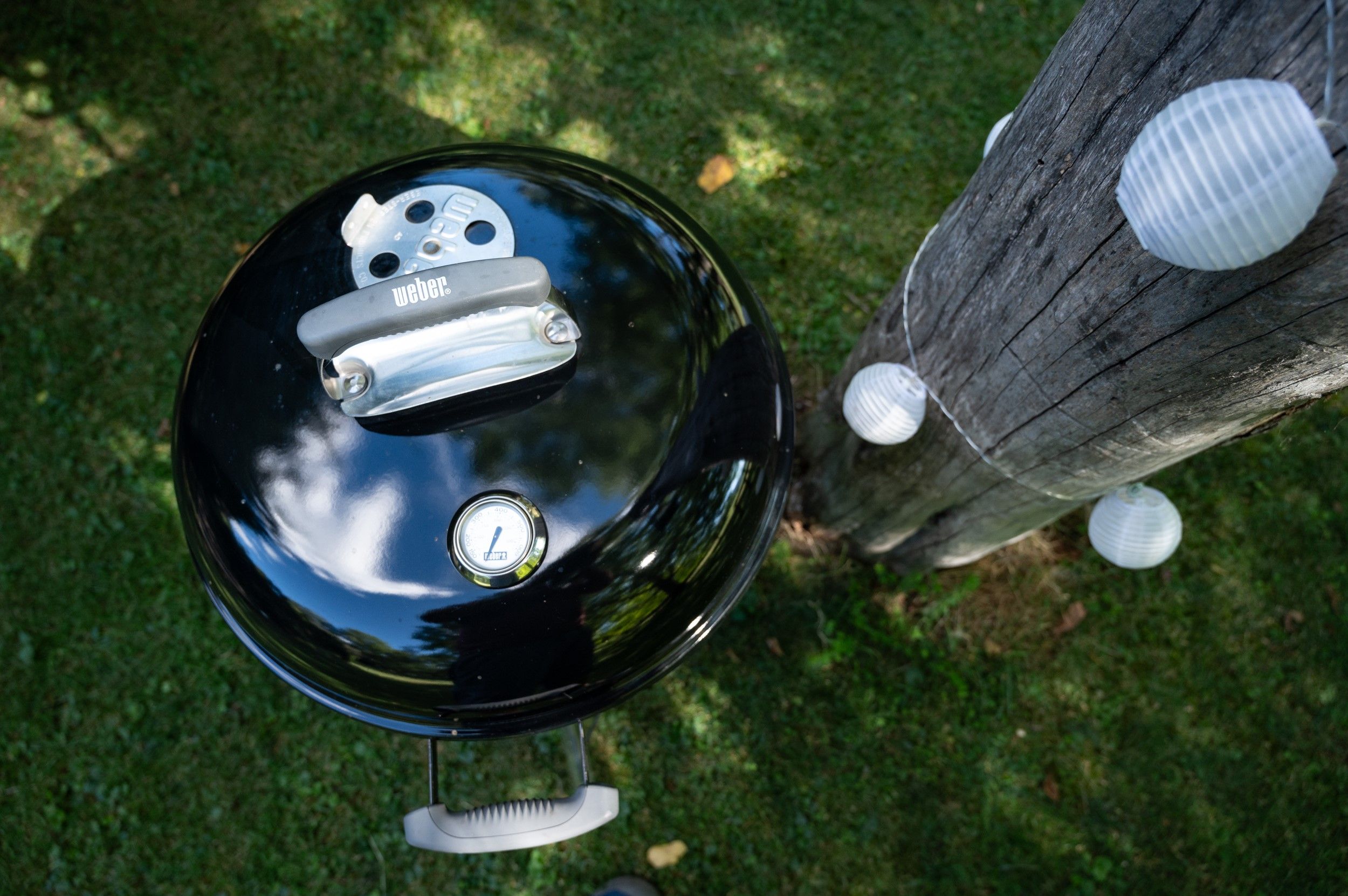 A kettle barbecue next to a tree trunk with fairy lights in the garden.