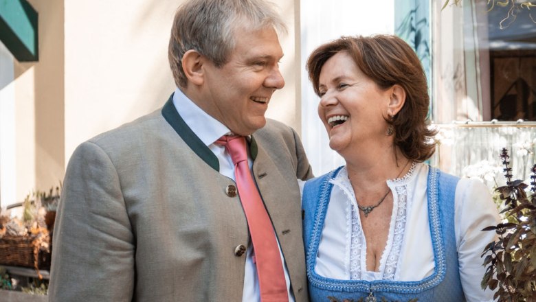 A man and a woman in traditional Bavarian dress laugh together.
