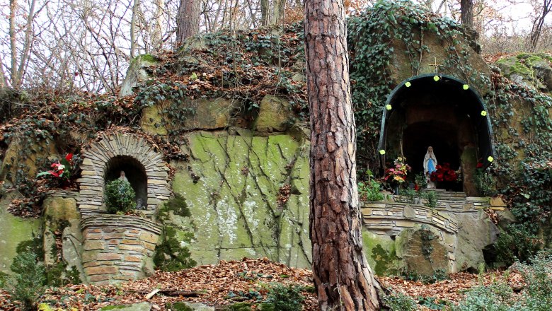 A stone grotto with a statue of the Virgin Mary and plants, surrounded by trees and foliage.