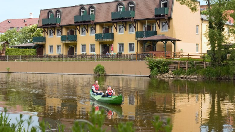 Two people in a canoe on a river in front of a yellow hotel.