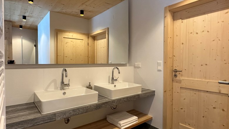 Modern bathroom with two washbasins, wooden ceiling and doors.