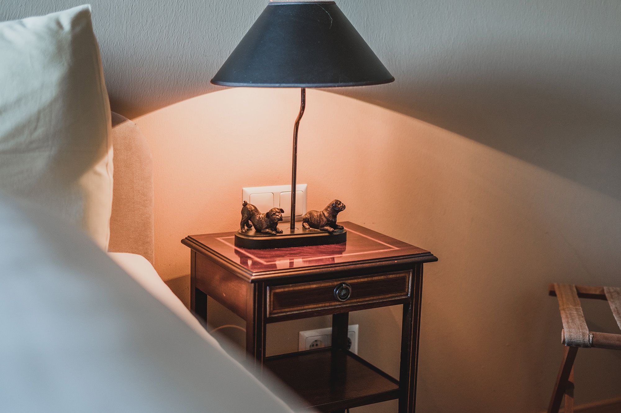 Bedside table with lamp and dog sculptures in a double room.