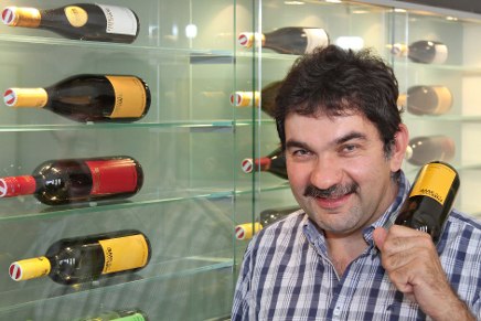 Man with a bottle of wine in front of a shelf with more bottles of wine.