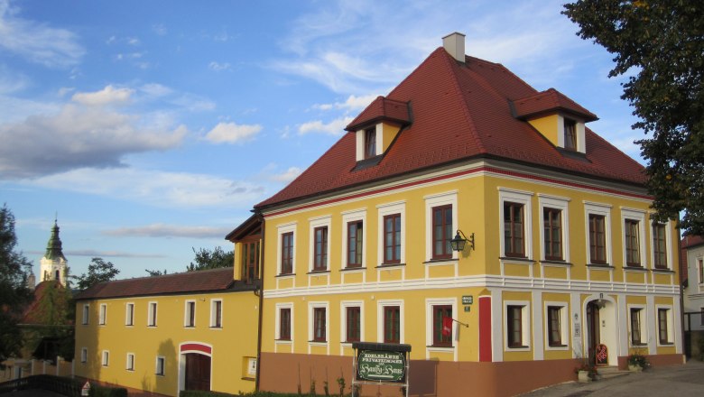 Hansy House, © Fam. Schrammel Yellow two-storey building with red roof and white window frames, next to it a smaller building. A church spire in the background.