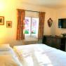 Comfortable double room with bed, TV, window with curtains, pictures on the wall and a small wardrobe.