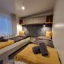 Two single beds in a cozy chalet room with yellow blankets and pillows, grey towels and a window with a curtain.