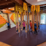 Children play in an indoor climbing room with a climbing wall and hanging elements.