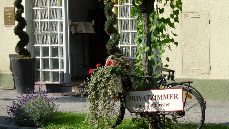Pension Hofmeister, © Familie Hofmeister Entrance to a guesthouse with a decorated bicycle and a sign for private rooms.