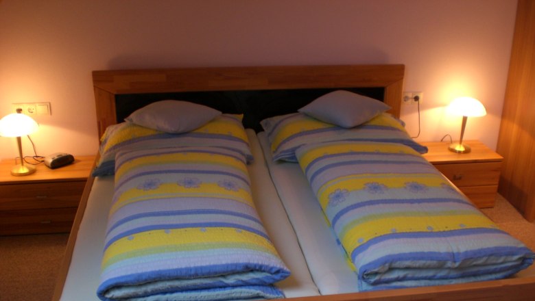 A cozy guest room with a double bed, colorful comforters and two bedside tables with lamps.