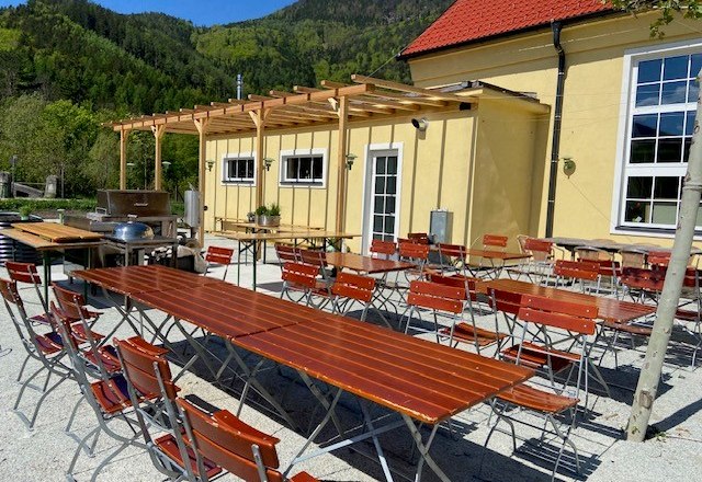 Beer garden with wooden tables and chairs in front of a yellow building.