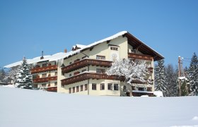 A large, traditional building in the snow with wooden decorations and a snow-covered tree in the foreground.