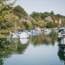 A quiet harbor with boats, surrounded by trees and a church tower in the background.