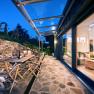 Terrace with wooden furniture and glass roof, view into the illuminated living room.