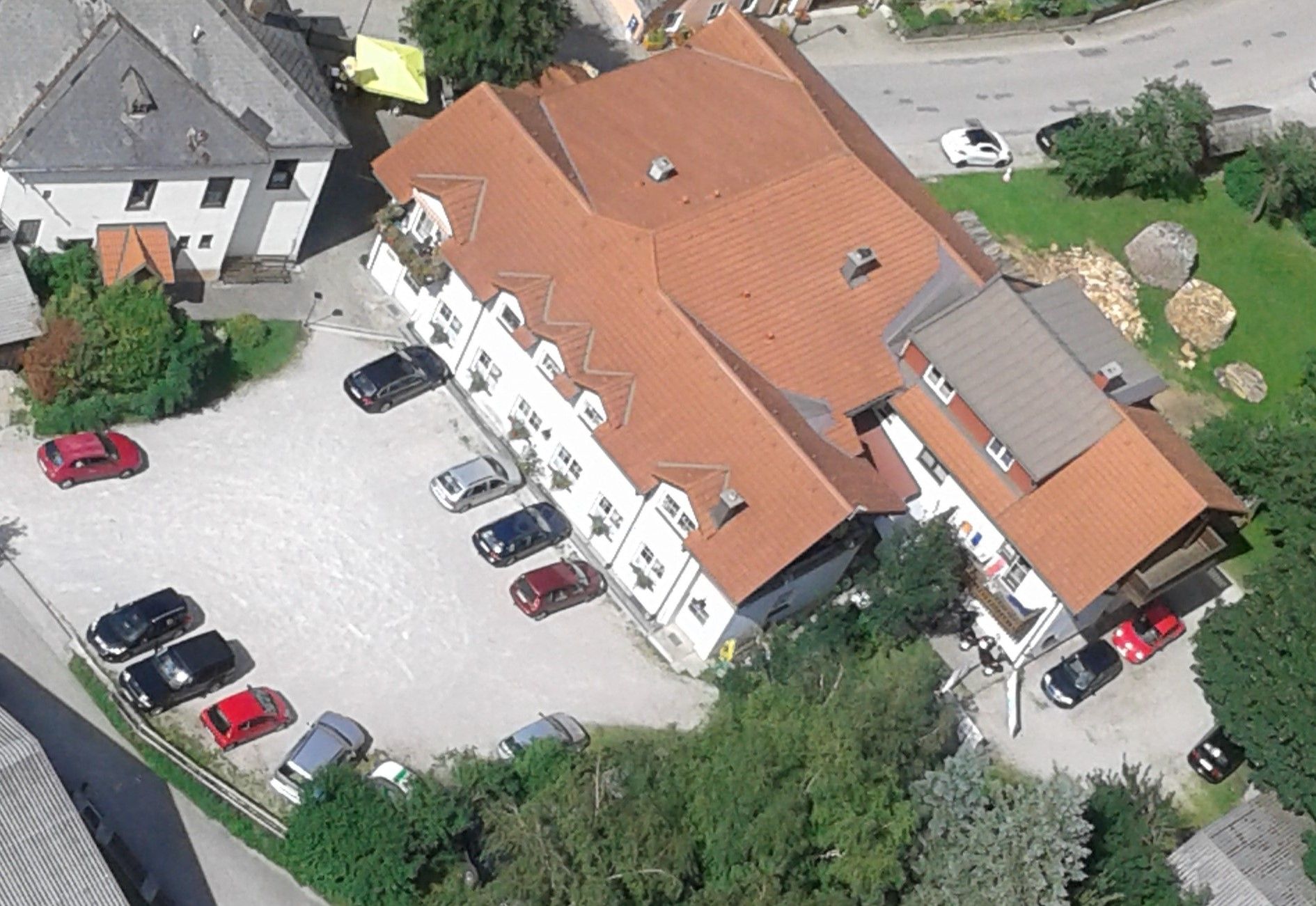 Aerial view of a building complex with red roofs and several parked cars in a parking lot.