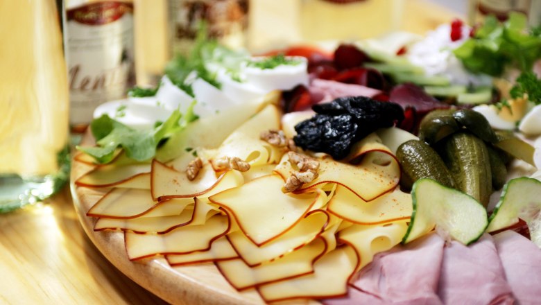 Snack board, © weinfranz.at A snack board with cheese, ham, gherkins, nuts and salad on a wooden table.