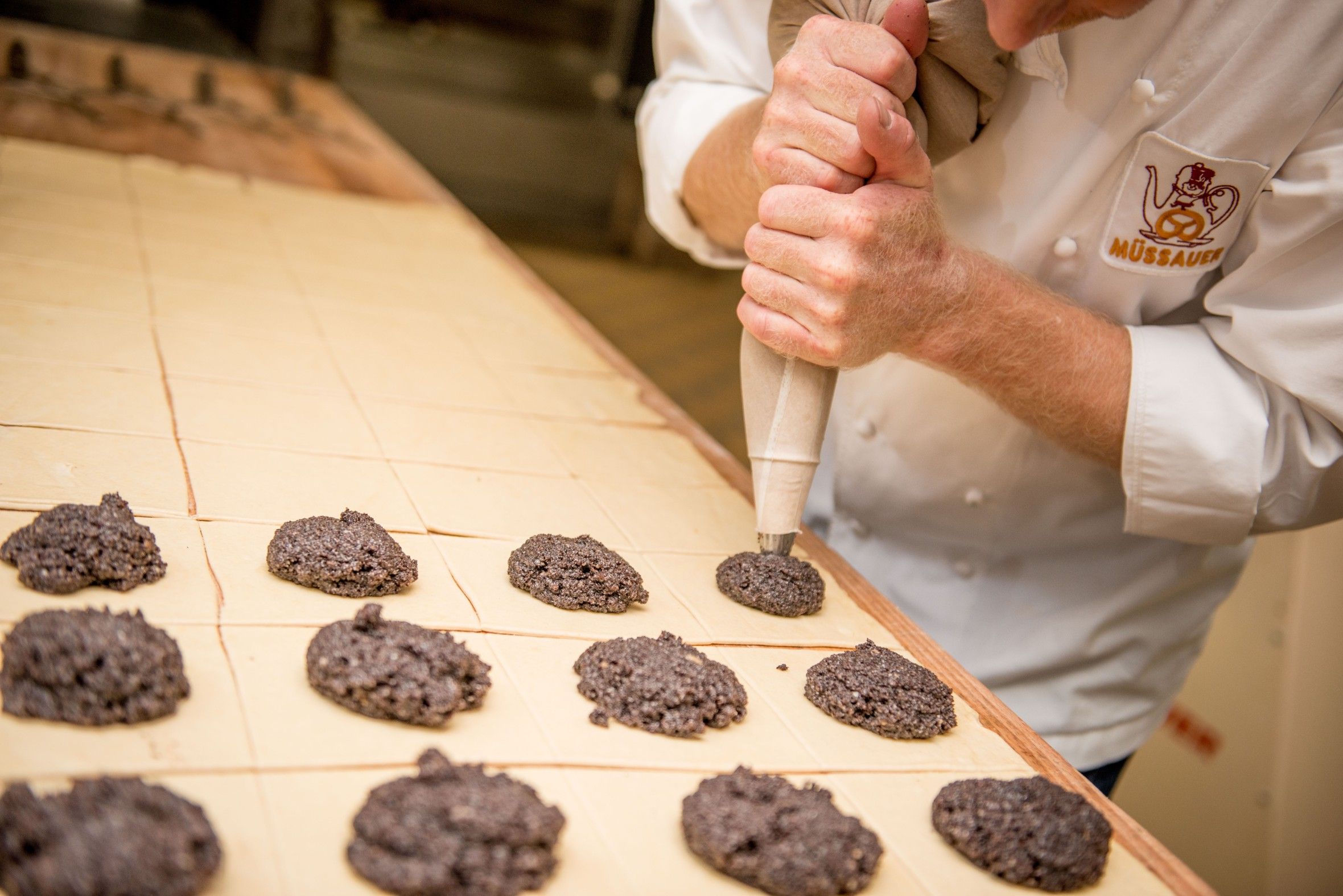 A baker sprays dough onto a baking tray in a bakery.