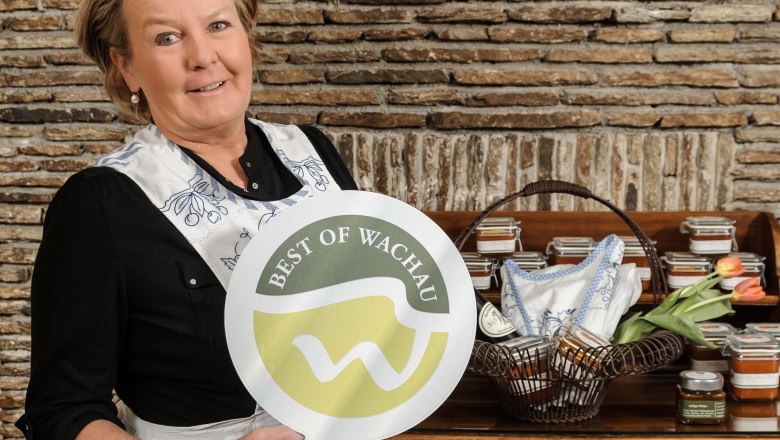 Lisl Wagner-Bacher holds a sign with the inscription 'Best of Wachau' in front of a stone wall.