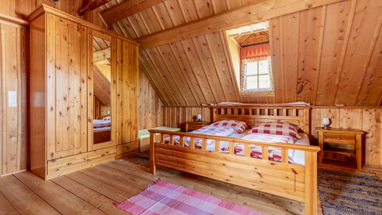 Bedroom with wood paneling, large double bed, wooden wardrobe, carpets and a window.