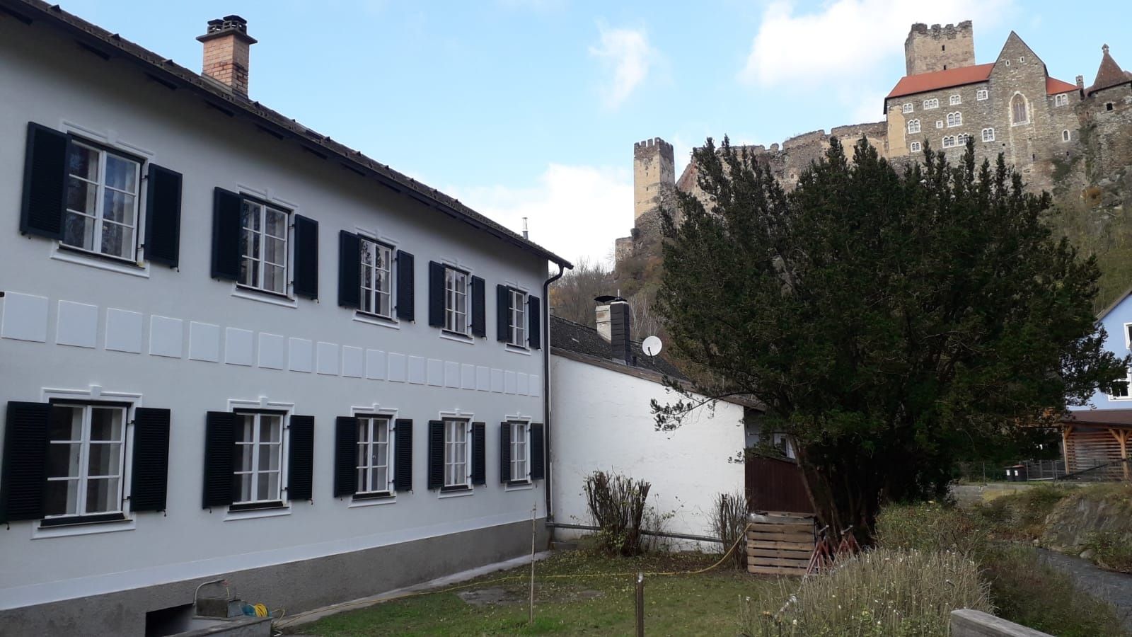 A white building with black shutters and a castle in the background.