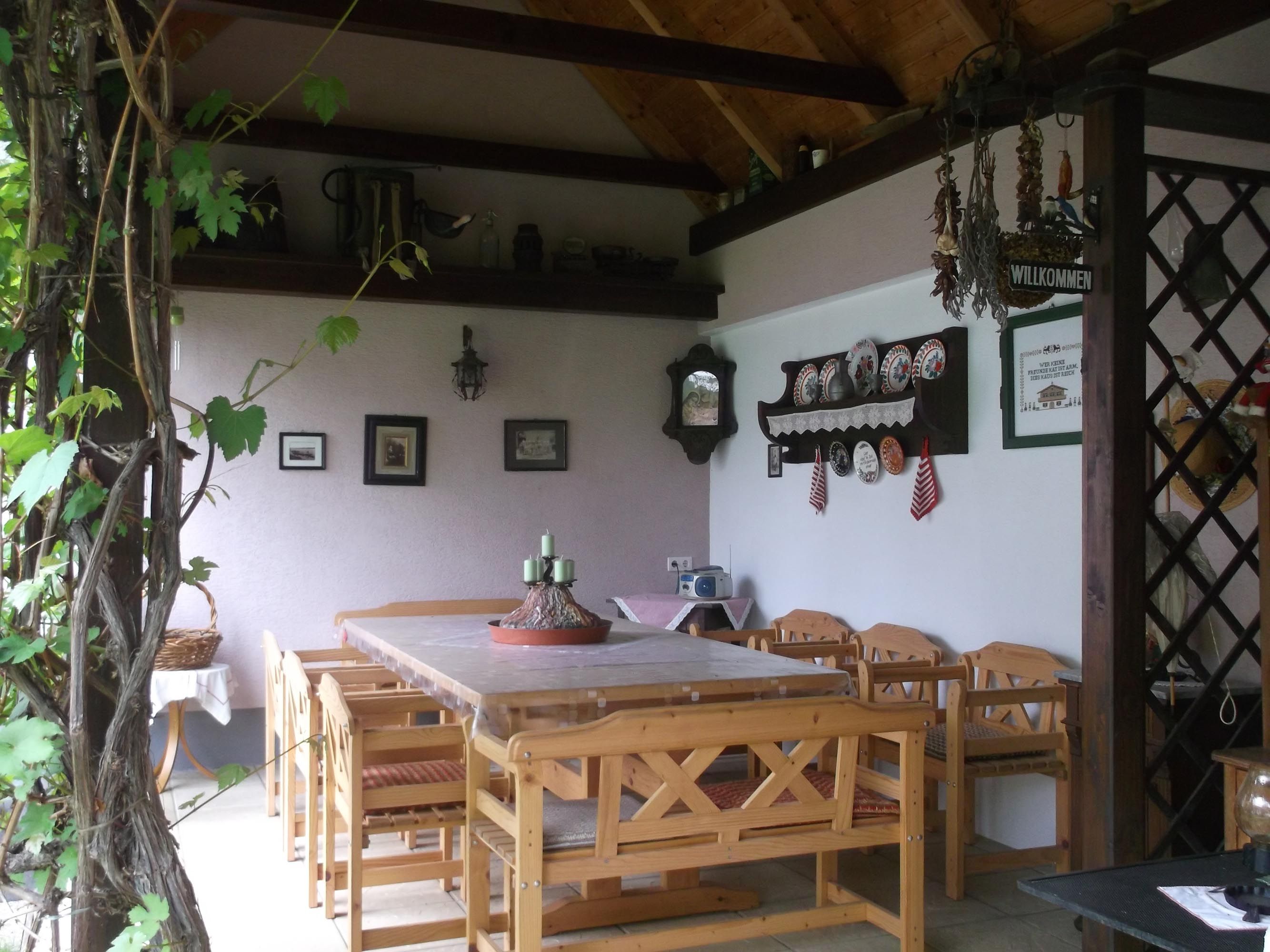 Covered terrace with table and chairs, in the background a wall with various wall decorations.