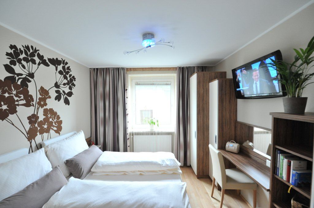 A modern bedroom with double bed, wall decoration, desk, TV and plants.