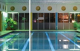 Interior view of an illuminated indoor pool with swimming pool and plants.