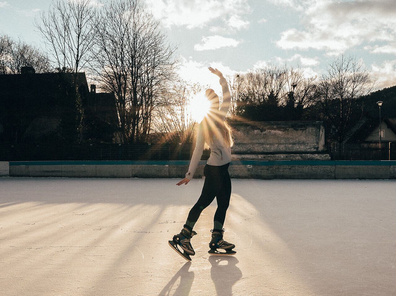 Ein strahlender Wintertag lädt zum Eislaufen ein, während die Sonne hinter den Bäumen aufgeht und eine magische Atmosphäre schafft. Die glitzernde Eisfläche spiegelt die warmen Farben des Himmels wider und verspricht unvergessliche Momente auf den Schlittschuhen.