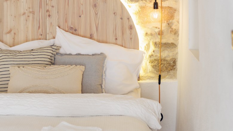 Cozy double bed with stone wall and wooden back wall, illuminated by a lamp.