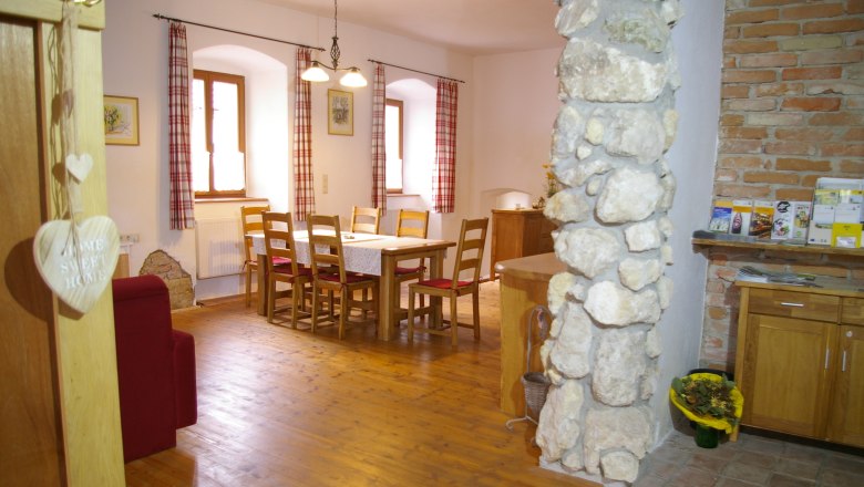 A warm welcome, © Fam. Zangl Cozy dining area with wooden table and chairs, red curtains and stone wall.