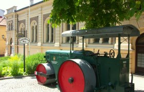Historic steamroller in front of a building with the inscription 'Siegfried Marcus Platz'.