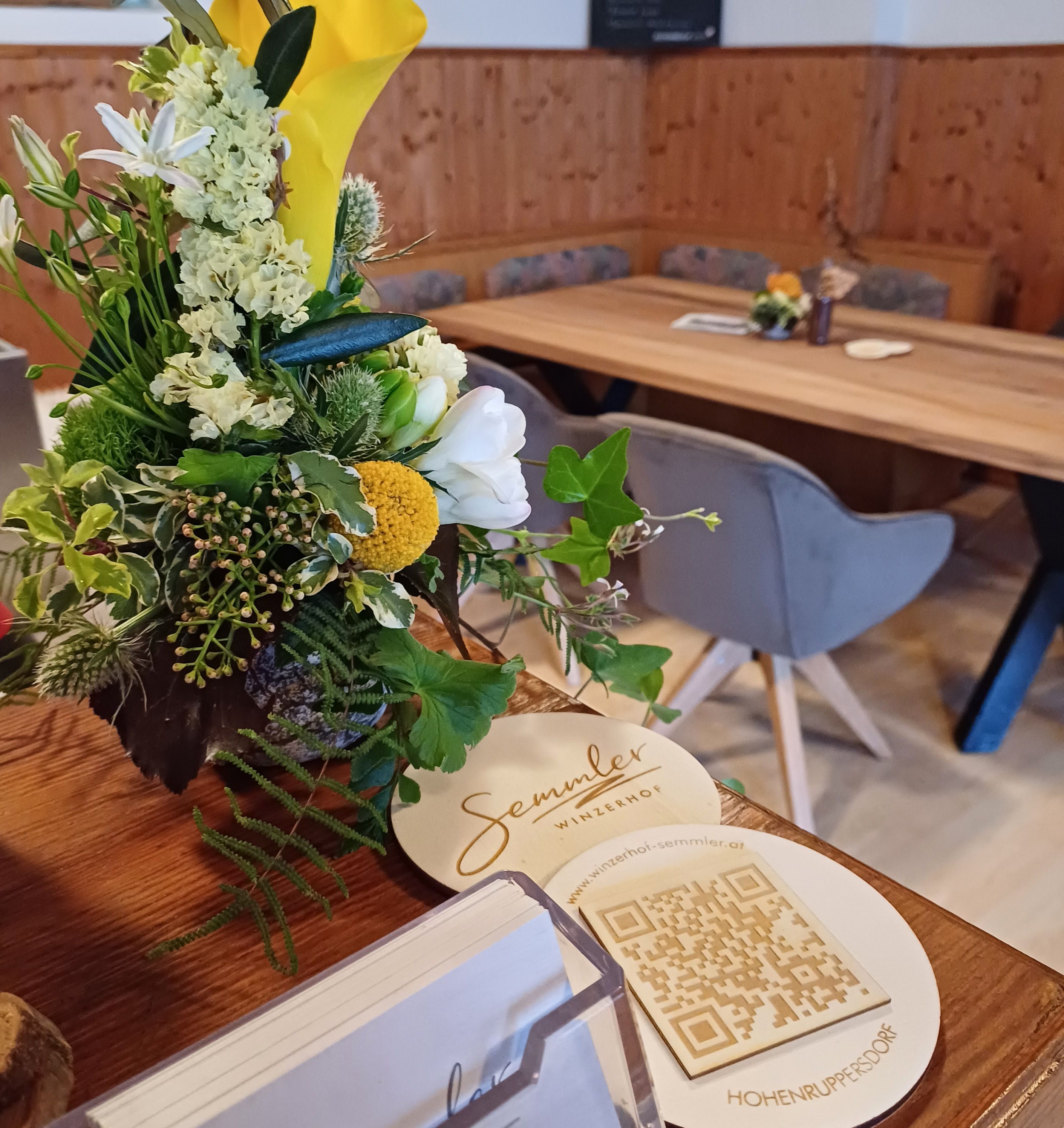 A flower arrangement on a table at Winzerhof Semmler with QR code and business cards.