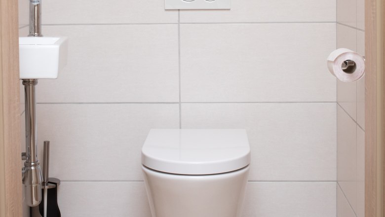 Modern bathroom with hanging toilet, small washbasin and toilet roll holder.