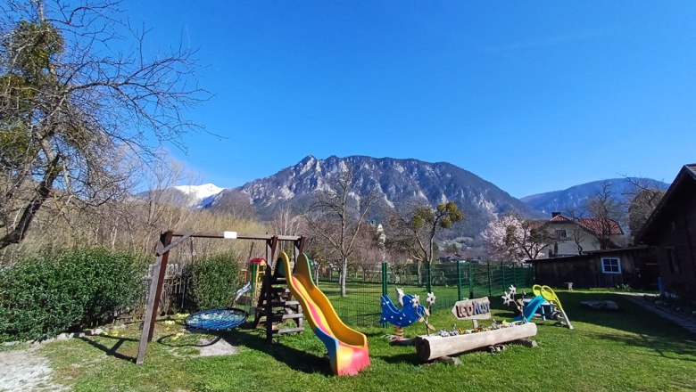 Children's playground with slide and swings against a mountain backdrop.