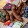 Close-up of sausages, grapes, tomatoes, cucumbers and onions on a wooden board.