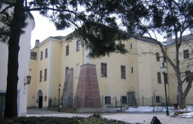 Purkersdorf Castle in winter with snow-covered ground and trees in the foreground.