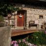 Rustic stone house with wooden door, bench and flowers in the foreground.