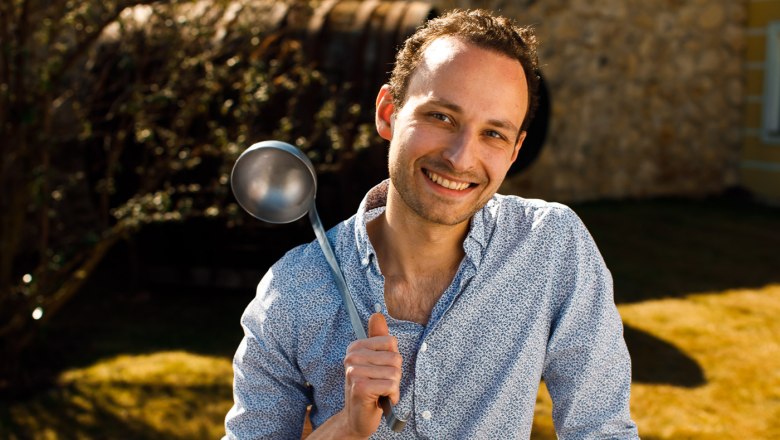 A smiling man outdoors holds a large ladle in his hand.