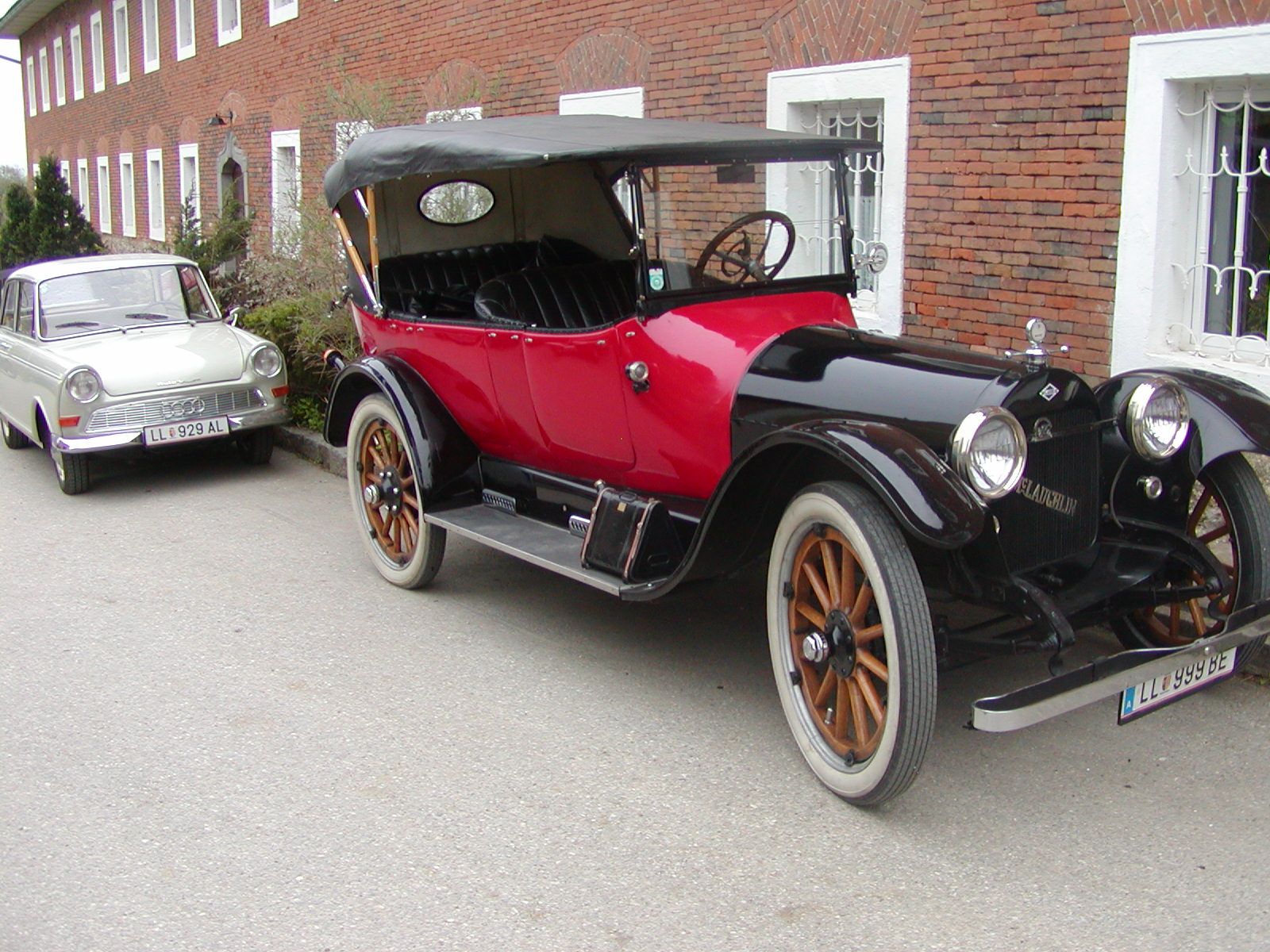 Two vintage cars parked in front of a brick building.
