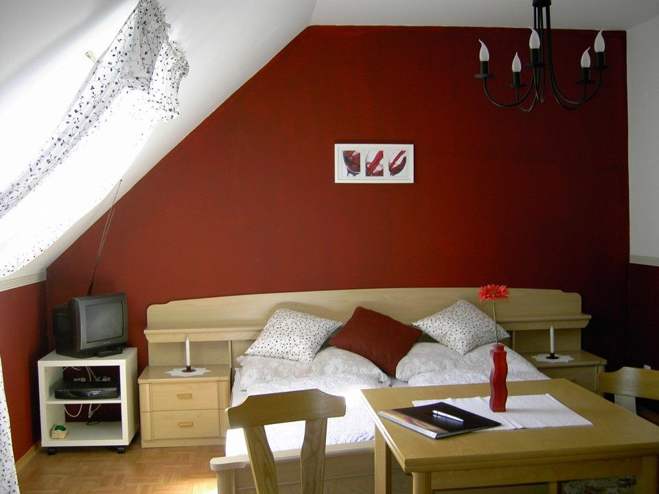 Cozy bedroom with red wall, bed, table and TV.