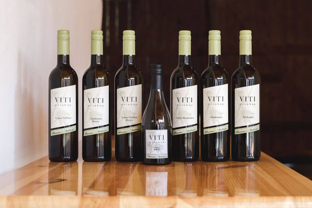 Seven bottles of wine on a wooden table, labeled 'VITI Weinbau'.