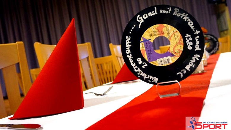 A festively laid table with a red tablecloth and napkins, decorated with a vinyl record as a menu card in the Stefan Hinger sports restaurant.