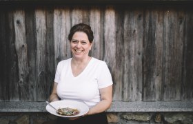 Woman in white T-shirt holding a plate of food in front of a wooden wall.