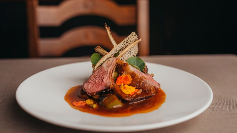 Gourmet dish with lamb, mini peppers, watercress and jus on a white plate.