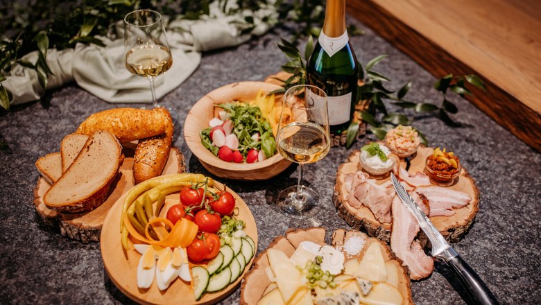 Various dishes on wooden plates with wine bottles and glasses.