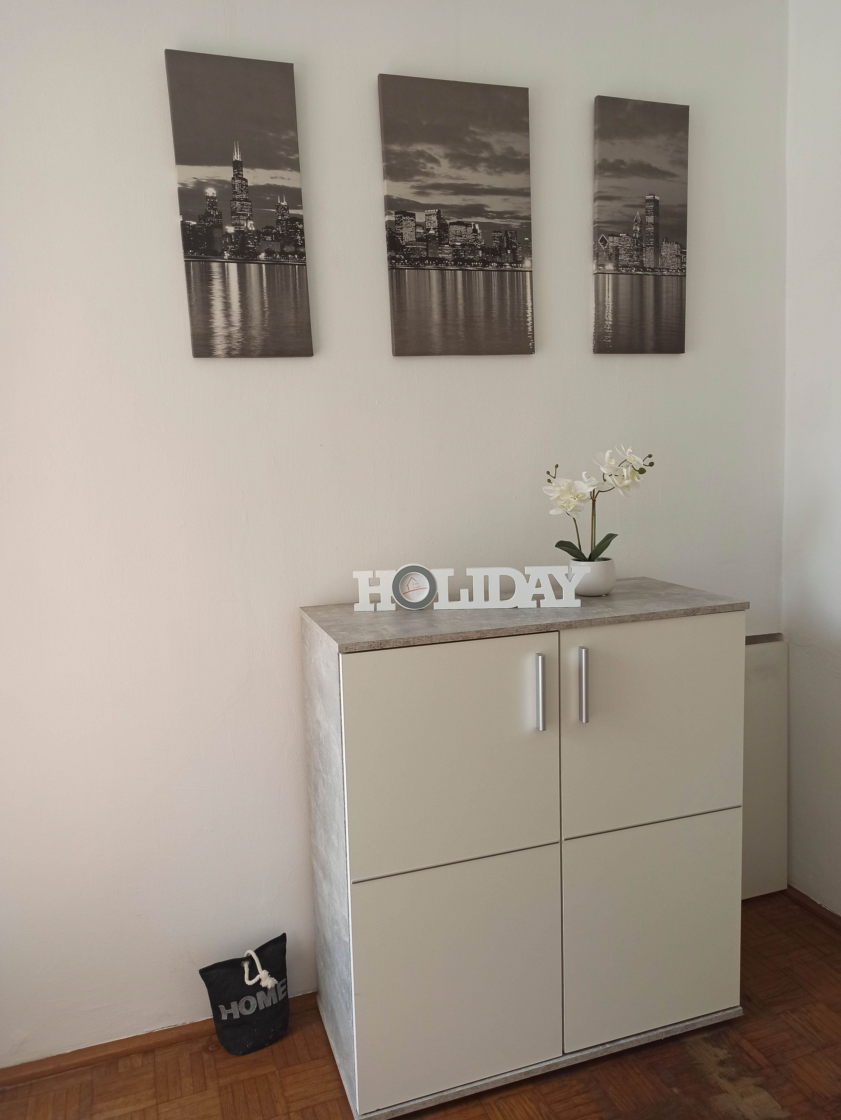 A white cupboard with decoration and three cityscapes on the wall.