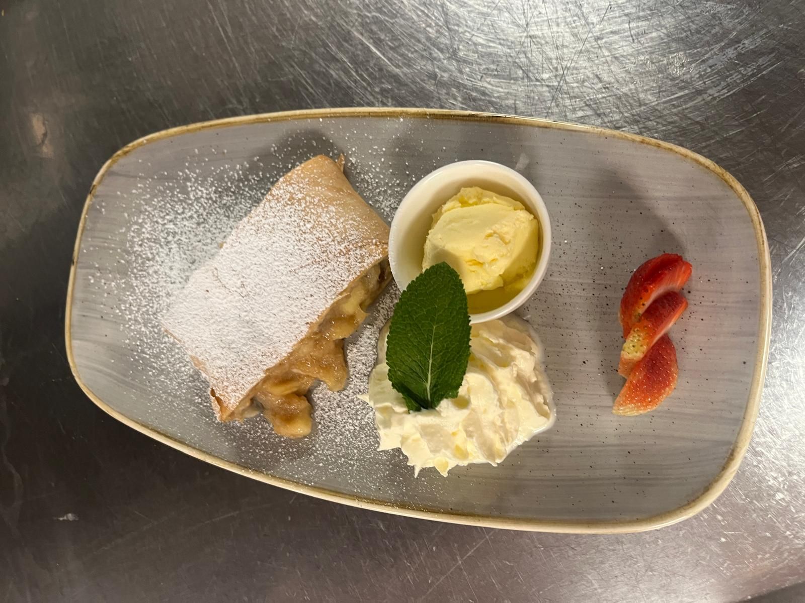 A dessert plate with apple strudel, vanilla ice cream, whipped cream and strawberry slices.
