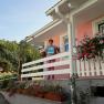 A person stands on a porch of a pink house with flowers and holds a sign.