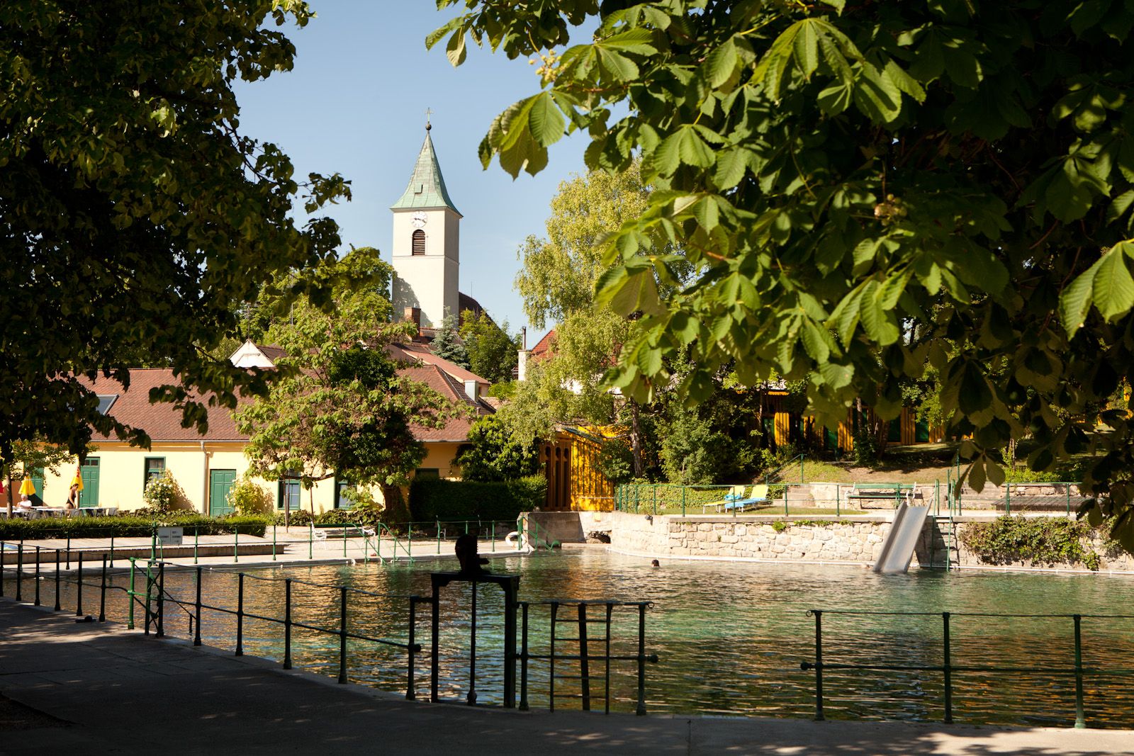 Bad Fischau-Brunn thermal baths with church in the background, surrounded by trees.