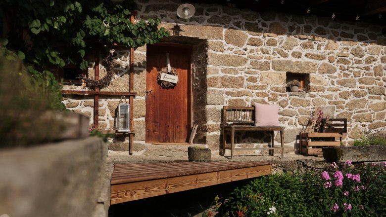Aigen13, © Mathias Lixl, lixl.com Rustic stone house with wooden door, bench and flowers in the foreground.